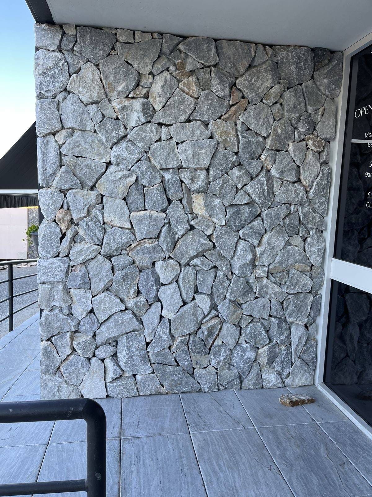 Grey natural stone exterior feature wall beside a glass entry door and paved surface