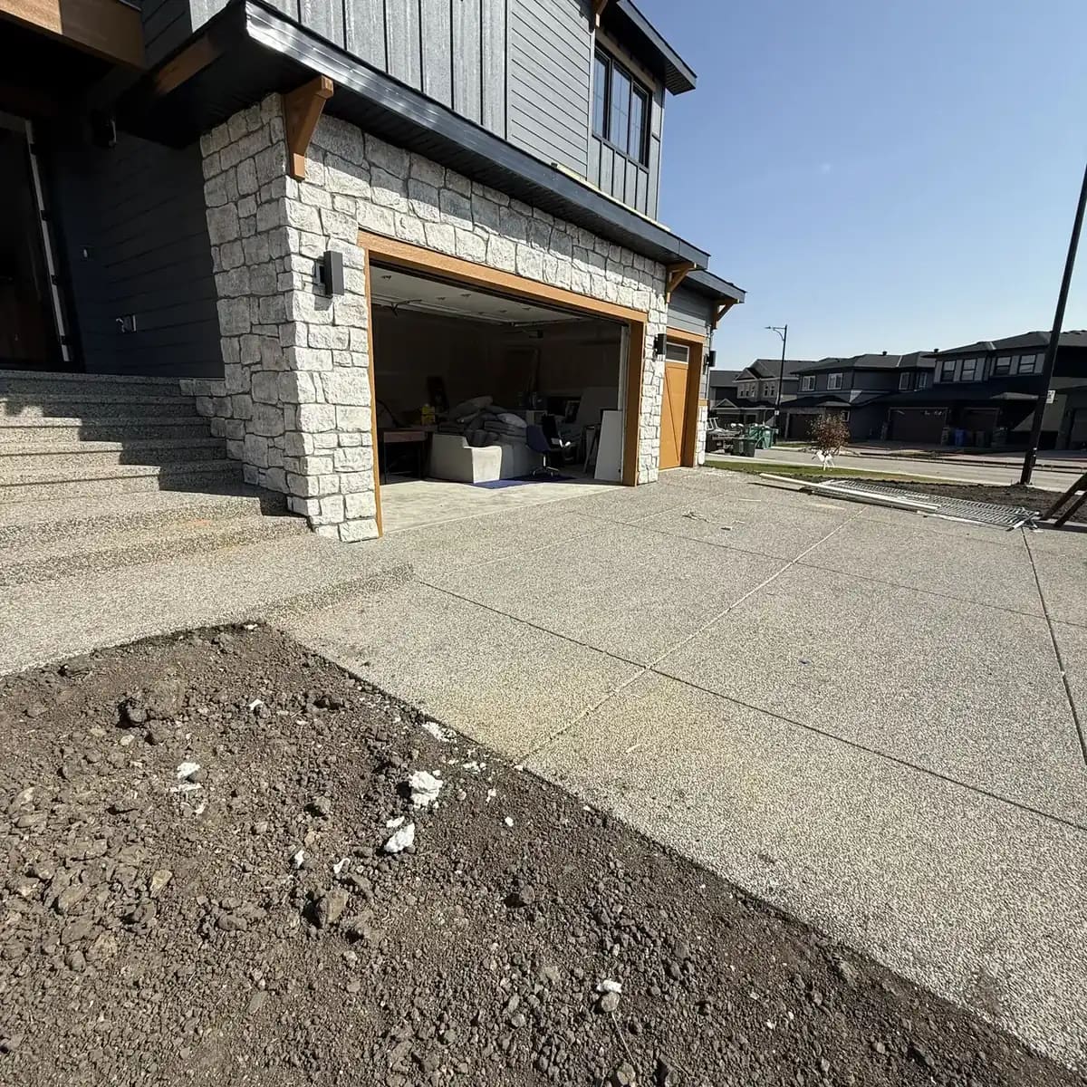 White stone garage corner with concrete flatwork, garage opening, and modern exterior trim
