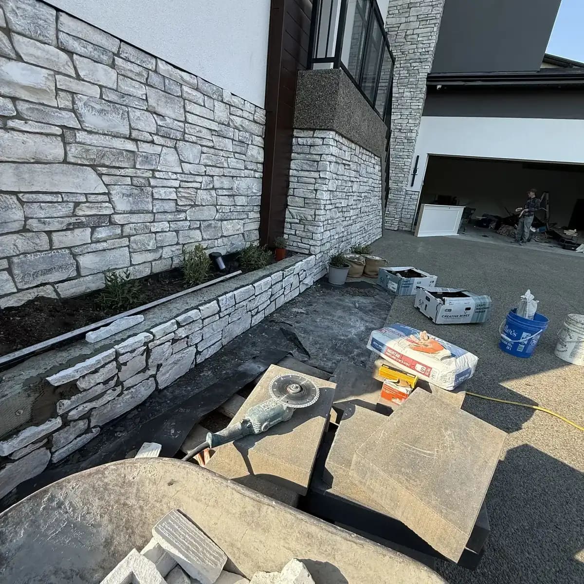 Concrete hardscape beside a white stone planter wall and exterior garage-side surface