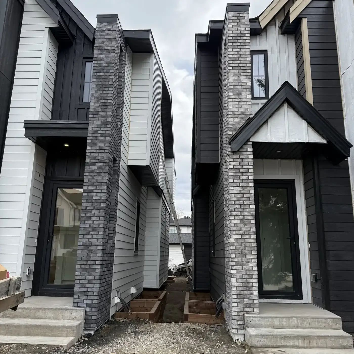 Modern residential exterior with tall grey stone masonry columns and black and white siding